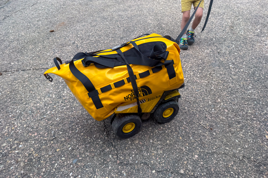 Yellow The North Face Base Camp Waterproof Duffel 50L being pulled on a toy dump truck across pavement.