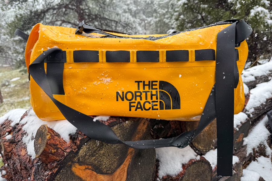 Yellow The North Face Base Camp Waterproof Duffel 50L sitting on a snowy log during wet-weather testing.