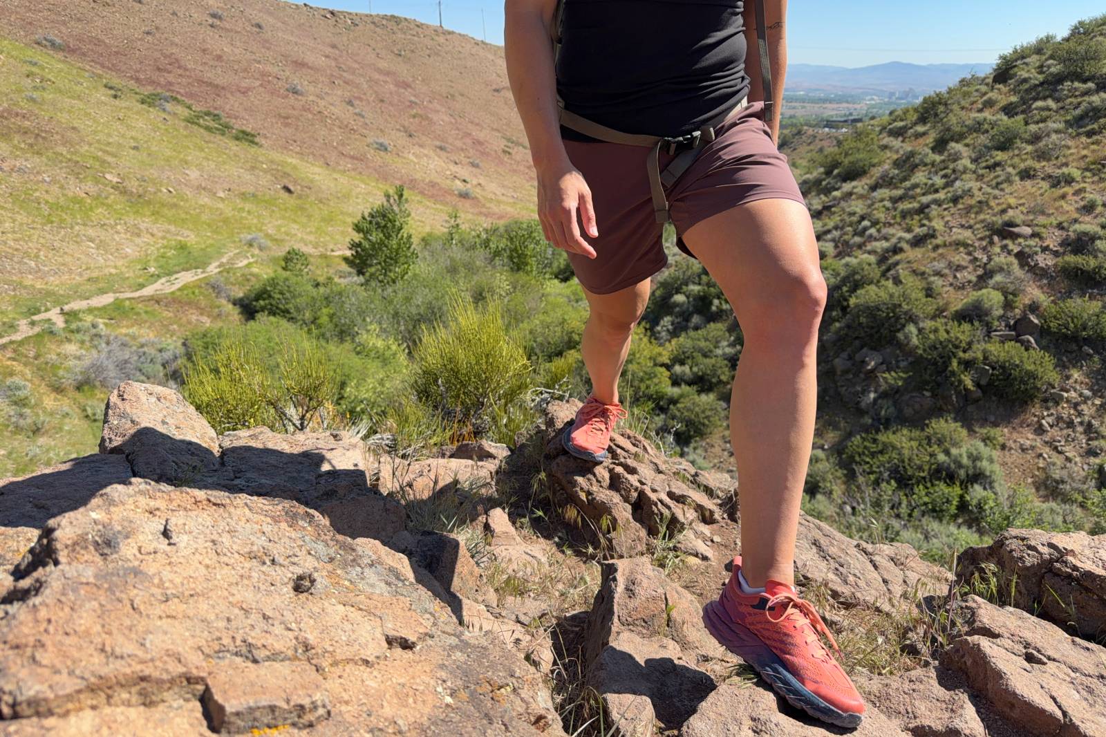 Close-up image of the bottom half of a woman wearing a pair of hiking shorts as she steps from one rock to another.