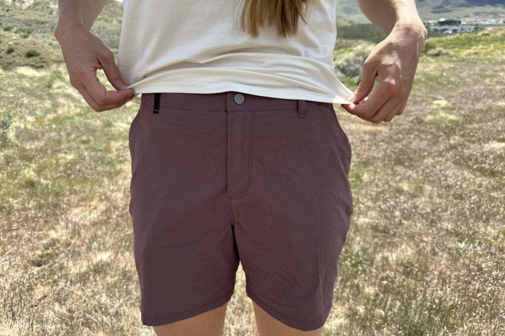 Close-up image of a woman holding up the bottom hem of her shirt to reveal the waistband on her hiking shorts.