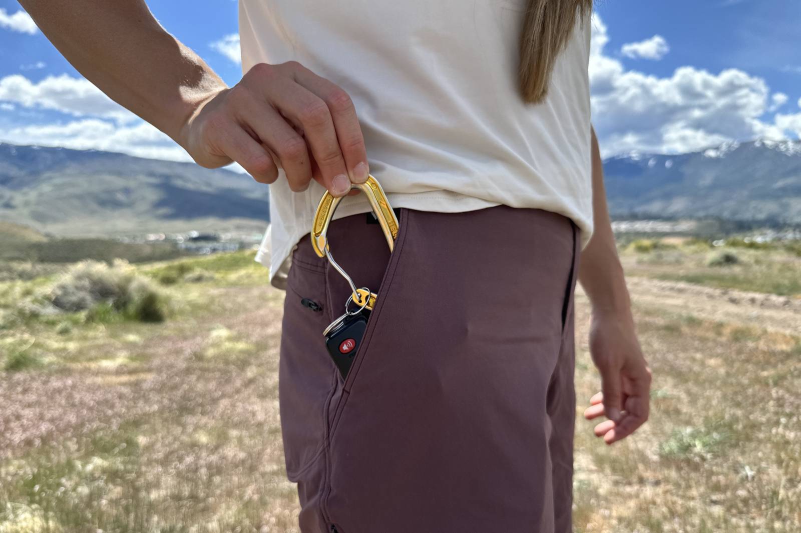 Close-up image of a woman reaching into the pocket of her hiking shorts to reveal a carabiner with keys attached.