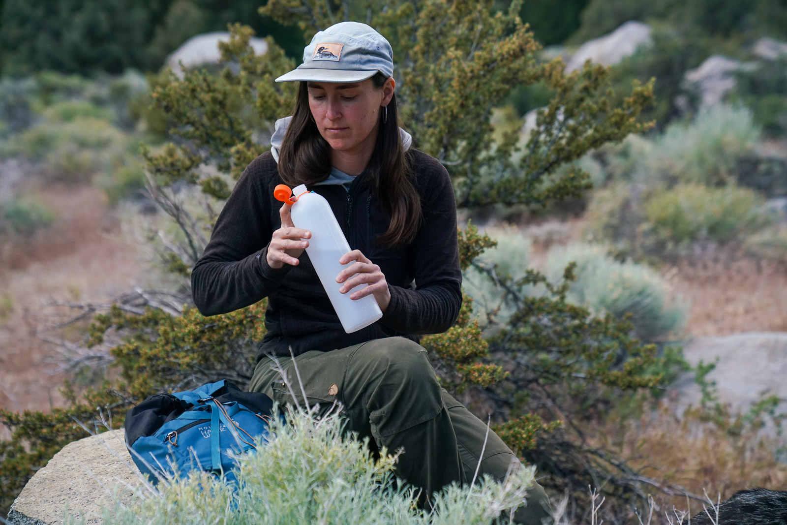 A person sitting on a rock opens a water bottle.