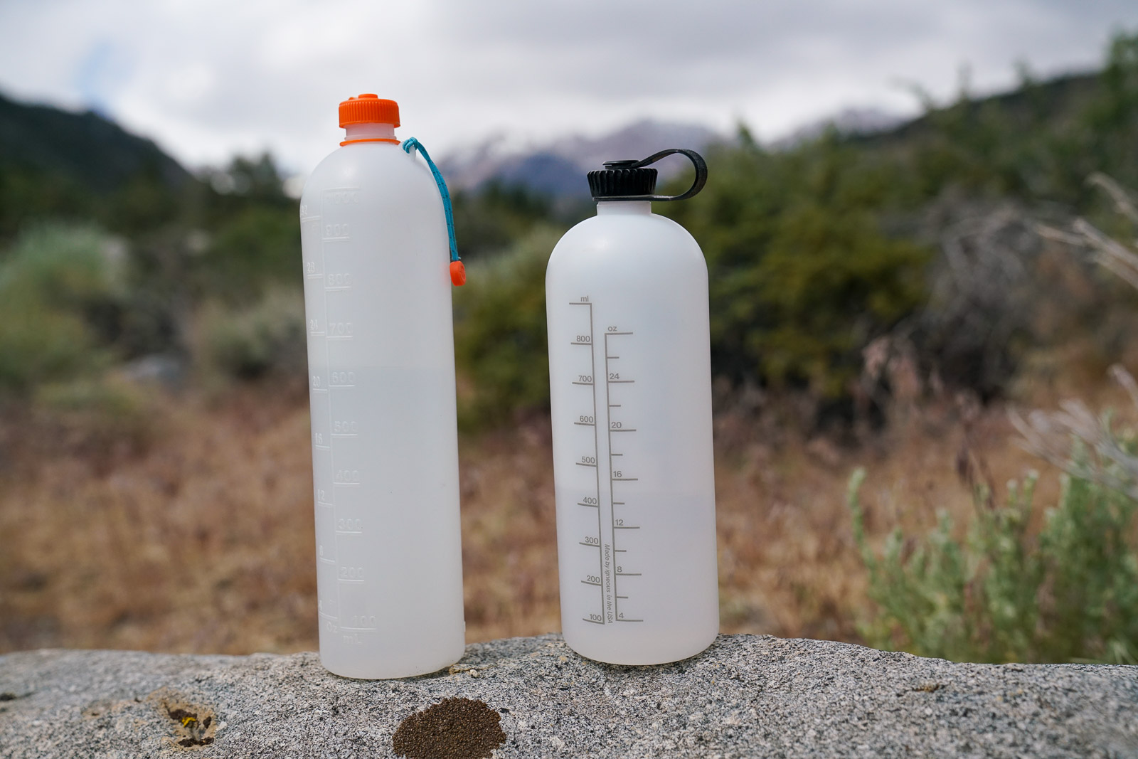 Two water bottle sit next to each other on a rock.