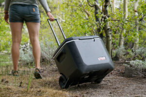 A person pulls a wheeled cooler along a forest path.