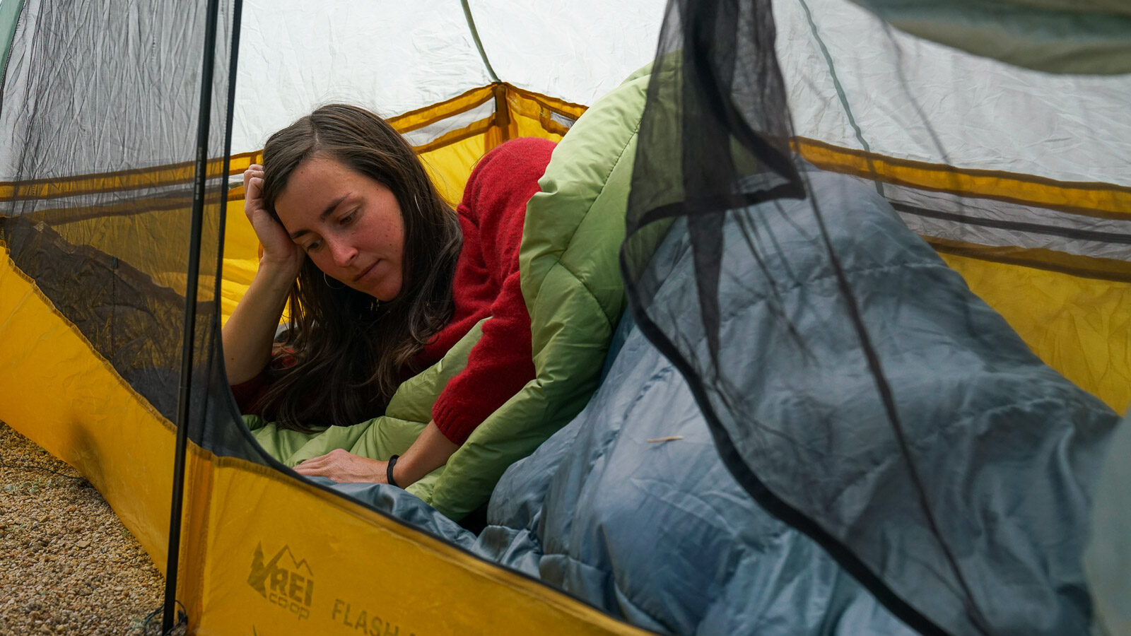 A person lays on their side in a sleeping bag inside a tent.