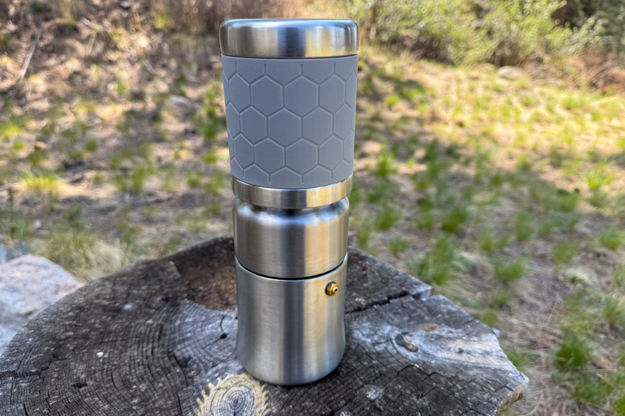 A coffee maker packed into its compact all-in-one form, standing upright on a tree stump at camp.