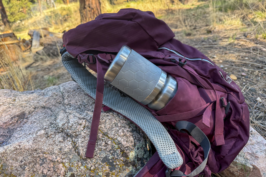 A packed coffee maker tucked into the side pocket of a backpack to show its trail-ready size.