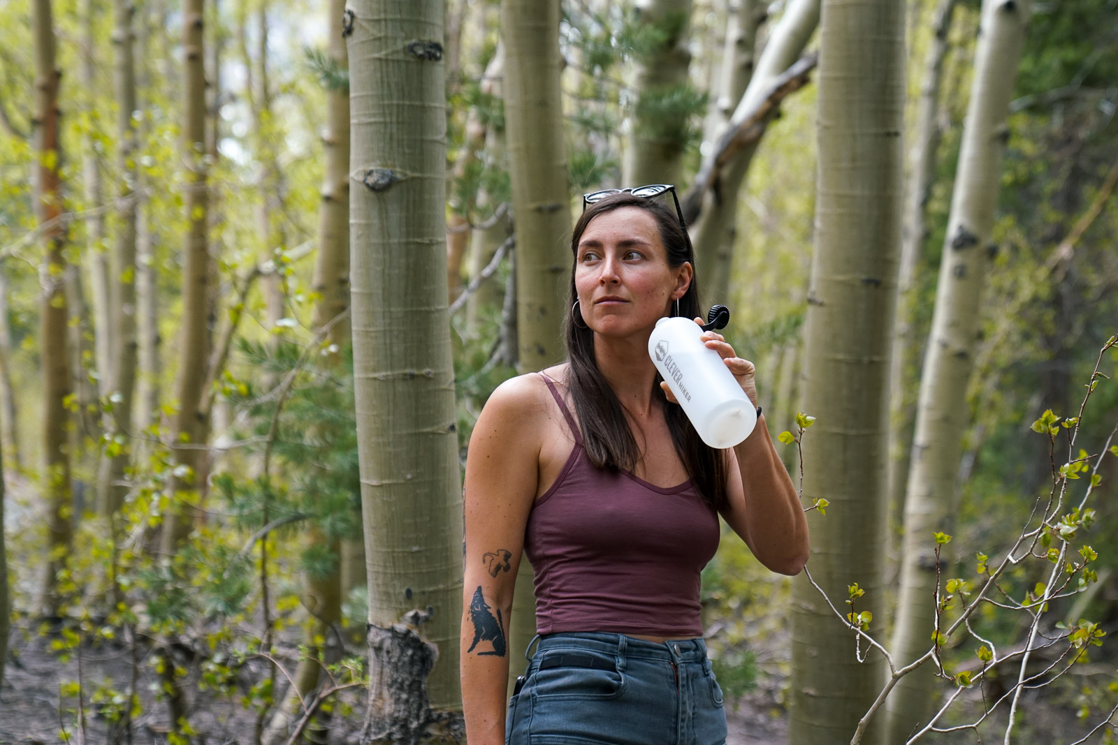 A person holds an open water bottle with a forest in the background.