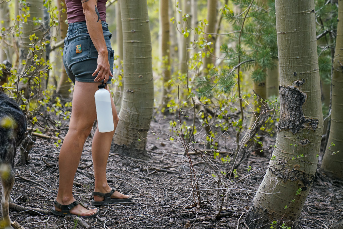 A person walks through a forest with a water bottle in hand.