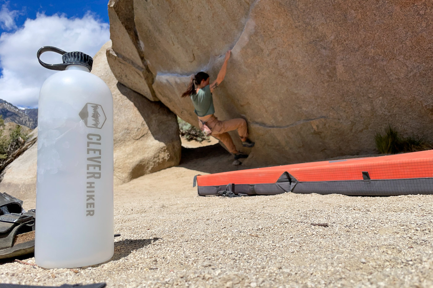A water bottle sits on the ground with a person bouldering in the background.