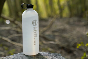 A water bottle sits on a rock with a forest in the background.