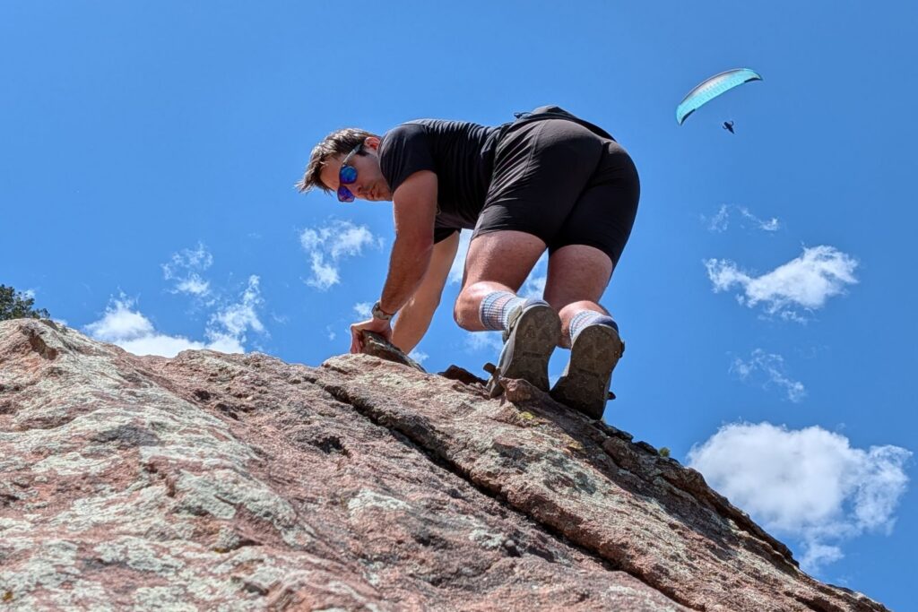 Scrambling in the flatirons in the Tread Lab Redway sandals with a paraglider flying above.