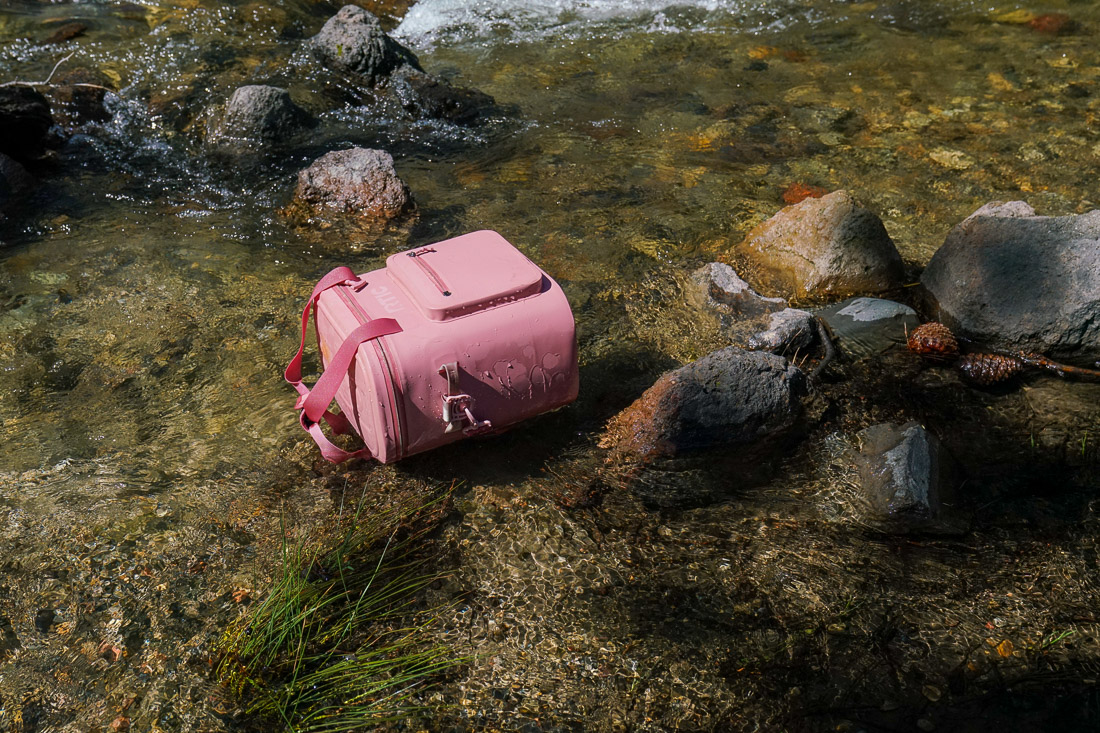 A soft-sided cooler floats in a creek.