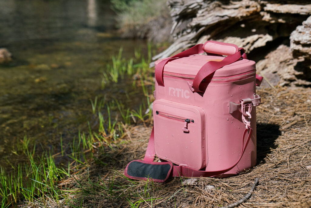 A wet soft-sided cooler sits next to a creek.