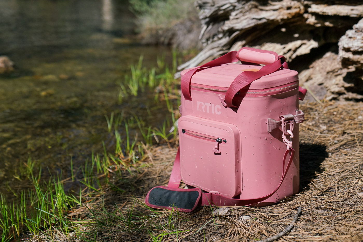 A wet soft-sided cooler sits next to a creek.