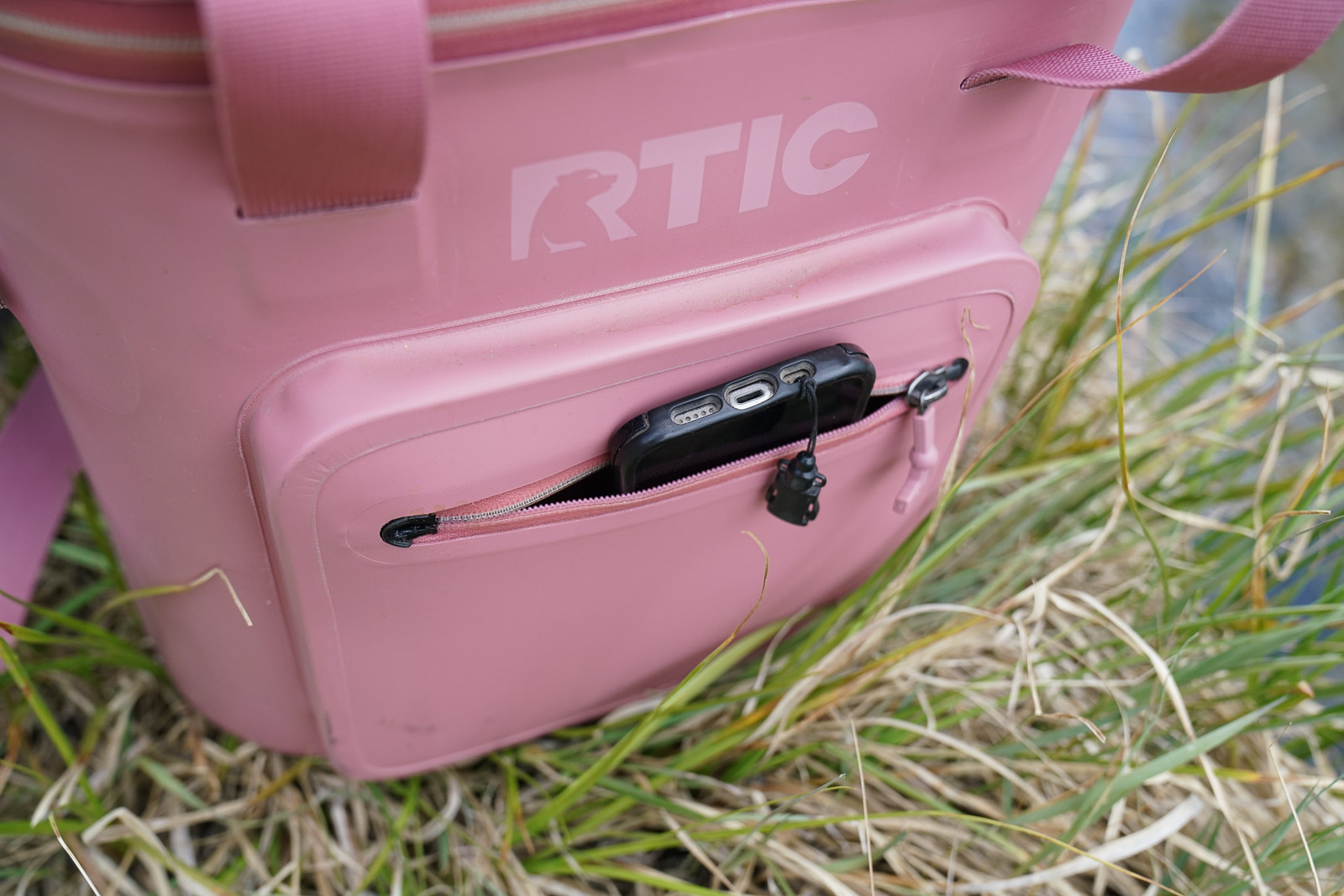A close up of a phone peeking out of the pocket of a soft-sided cooler.