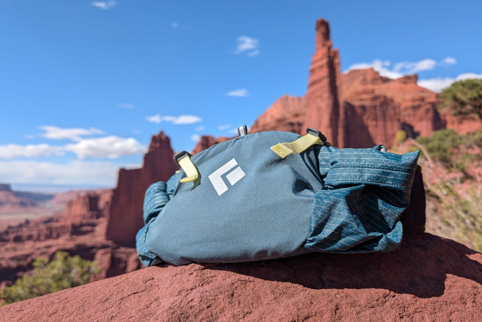 A blue lumbar pack sits on red dirt with a view of desert towers in the background.