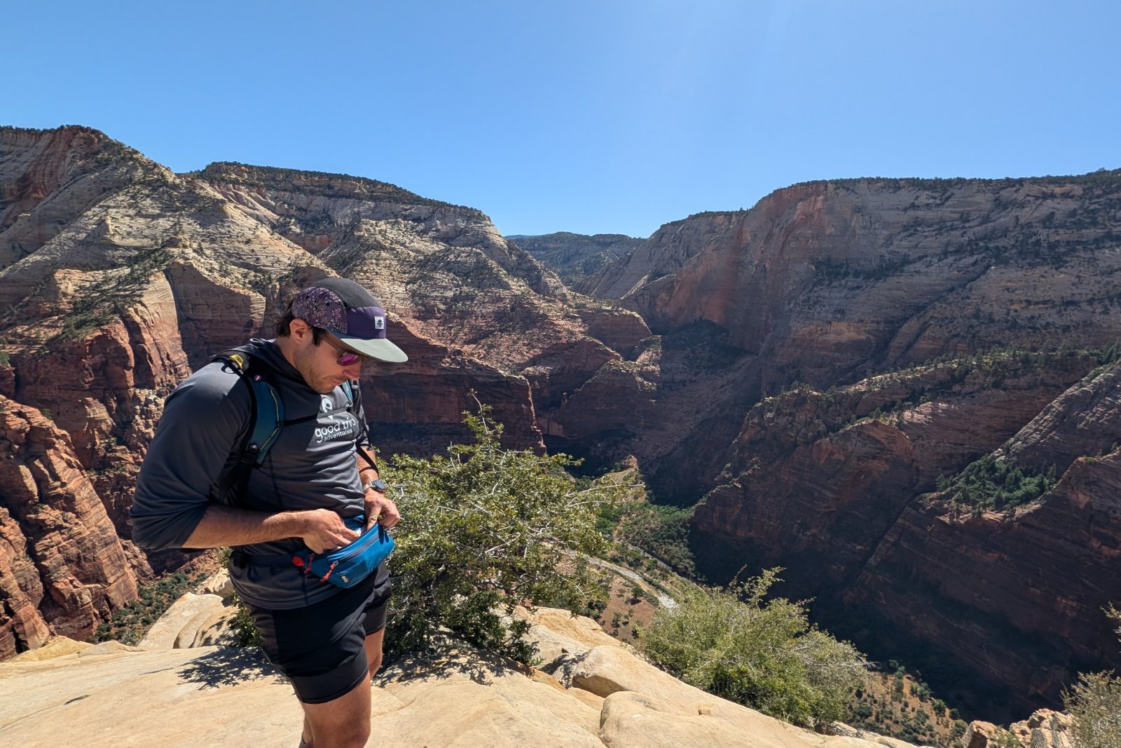 Searching for a snack in a blue fanny pack while standing on top of a rocky outcropping overlooking Zion National Park.