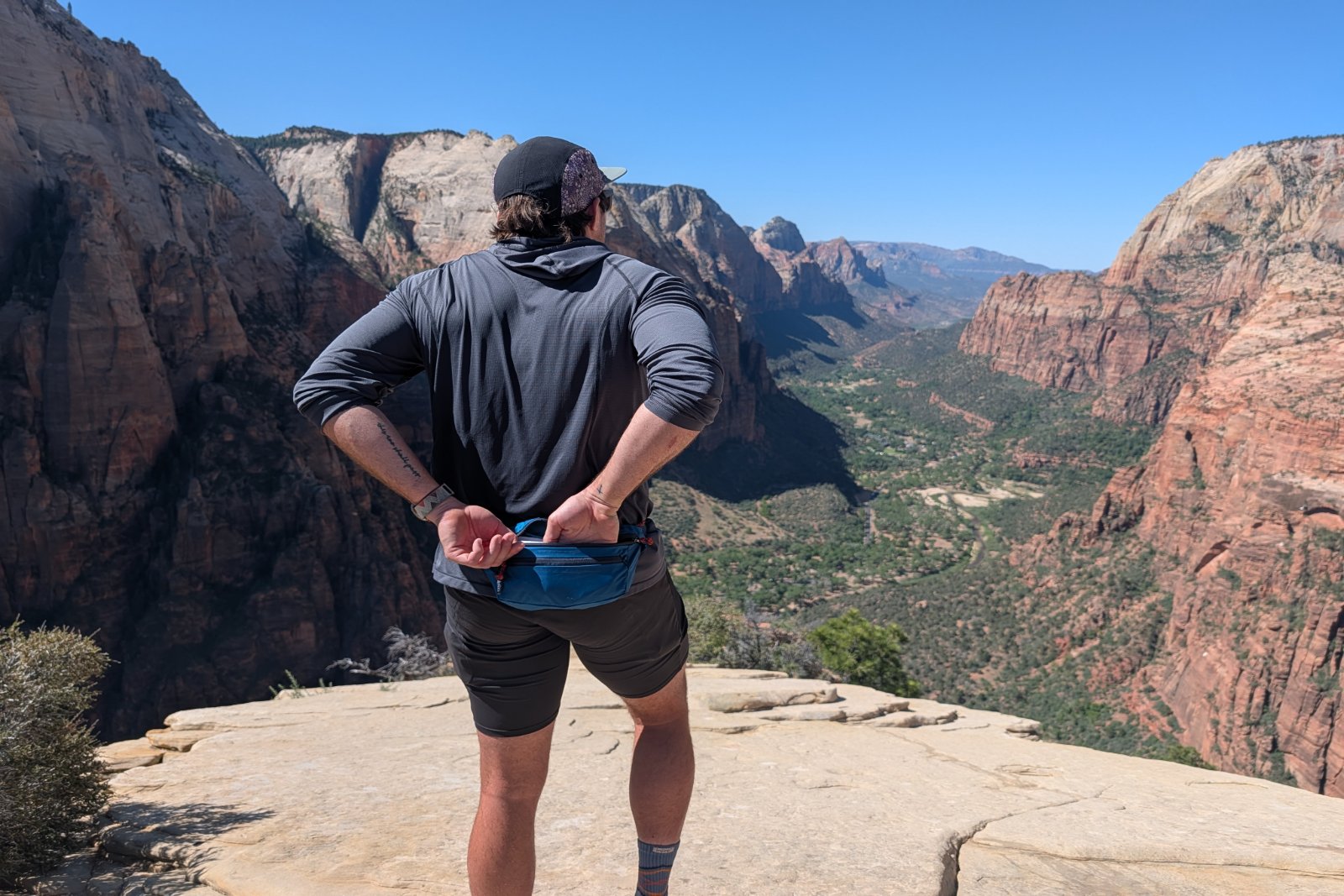Reaching into a blue fanny pack while overlooking red rocks and greenery in Zion National Park.