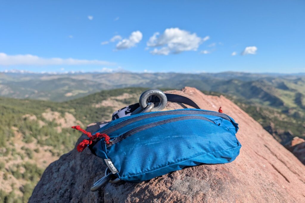 A blue fanny pack sits on top of a rappel bolt with a view of Boulder, Colorado in the background.