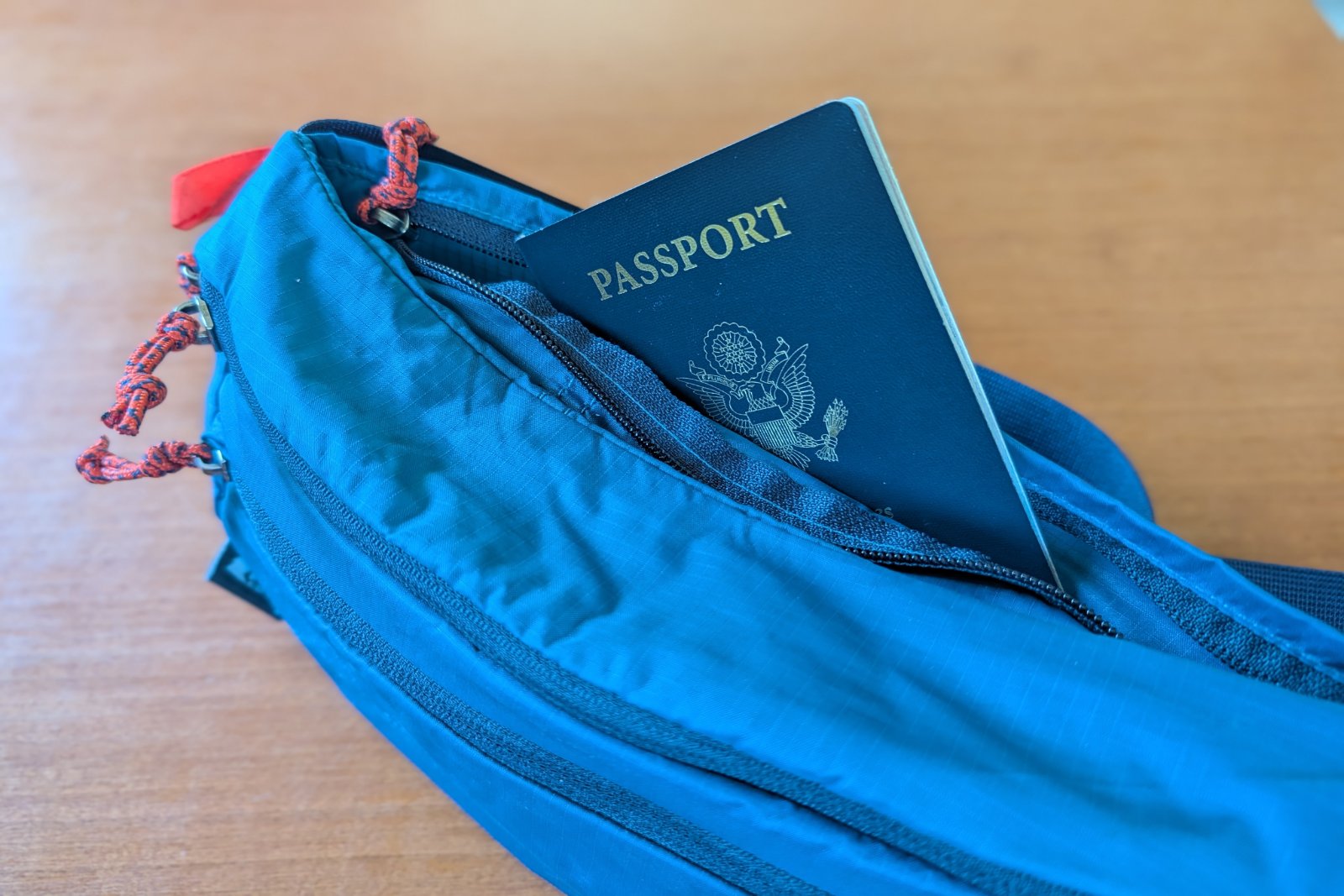 A passport popping out of the hidden pocket of a blue fanny pack.