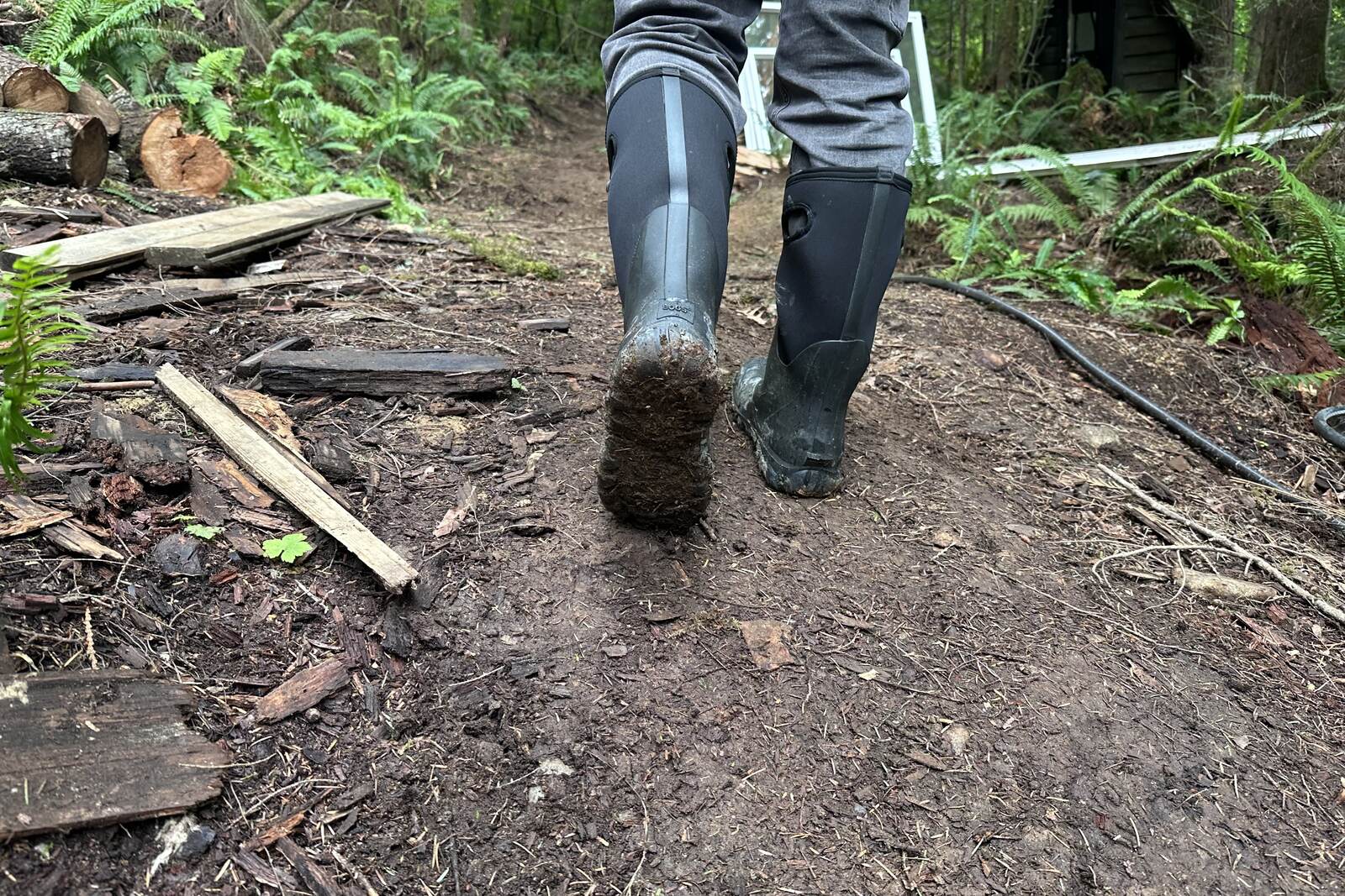 Close up of tall black rubber rain boots walking in a muddy building site.