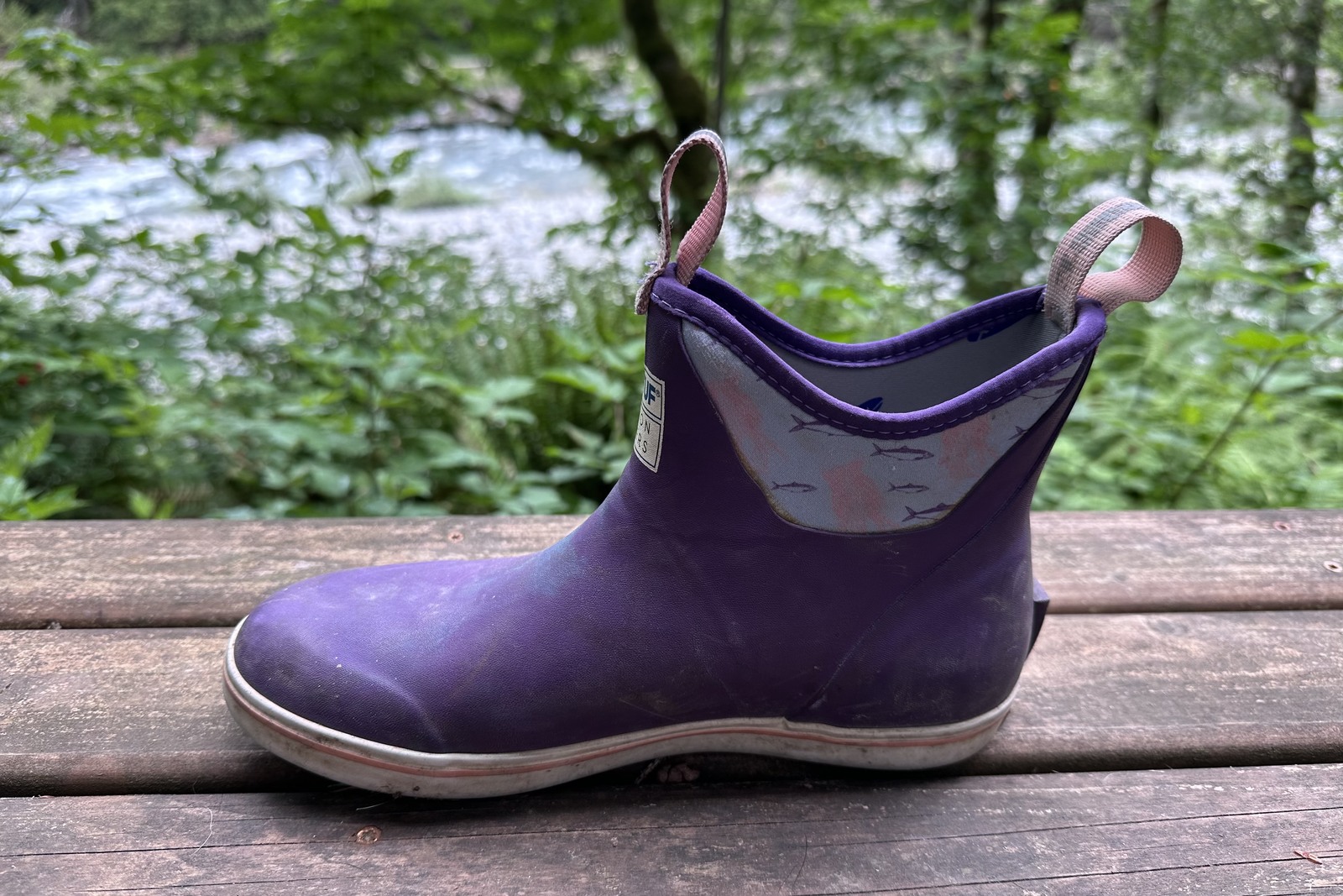Close up of a purple ankle rain boot on a wooden porch with a forested background
