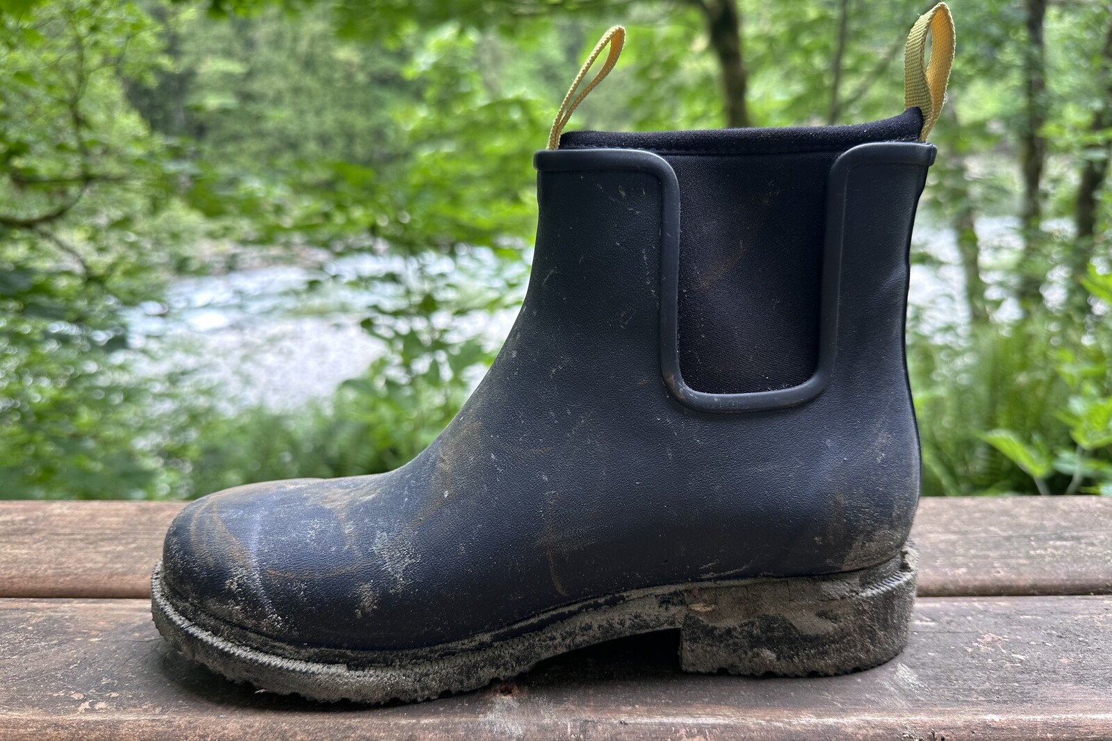 Close-up of a navy ankle boot on a wood porch with a forested background.