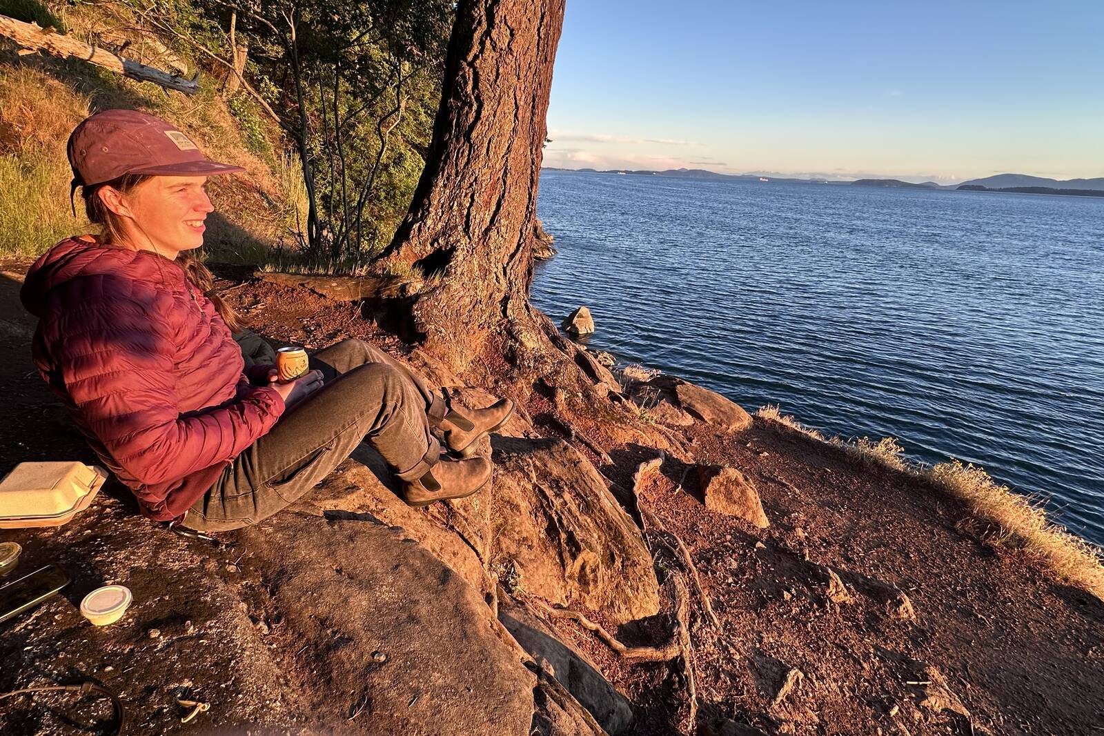 A person is sitting on a rock overlooking a large body of water at golden hour.