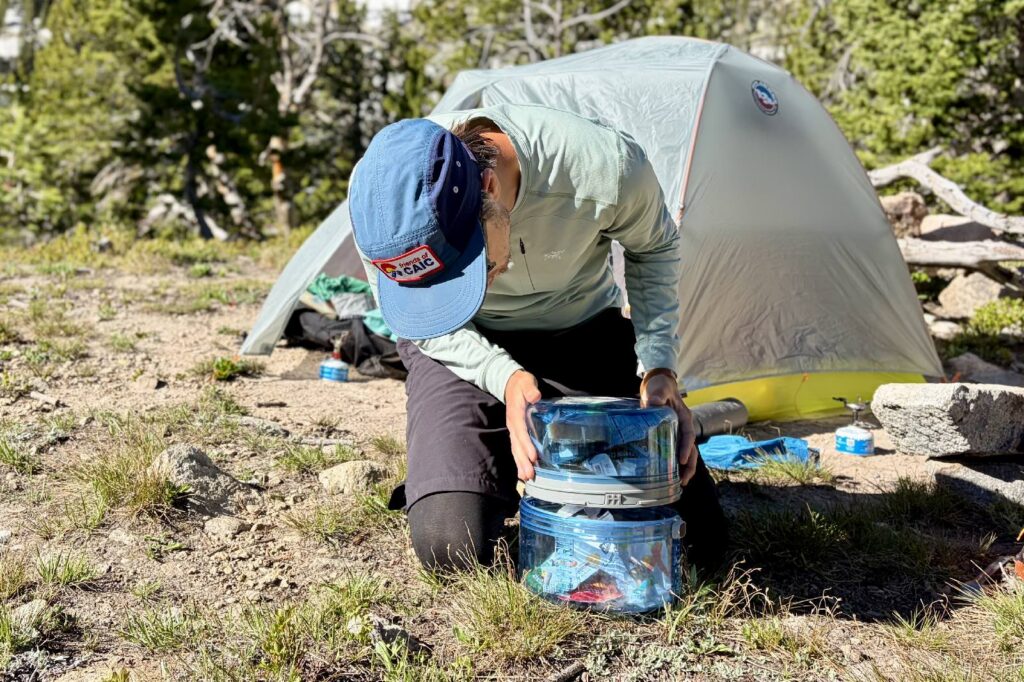 A hiker screws together two halves of a bear canister.