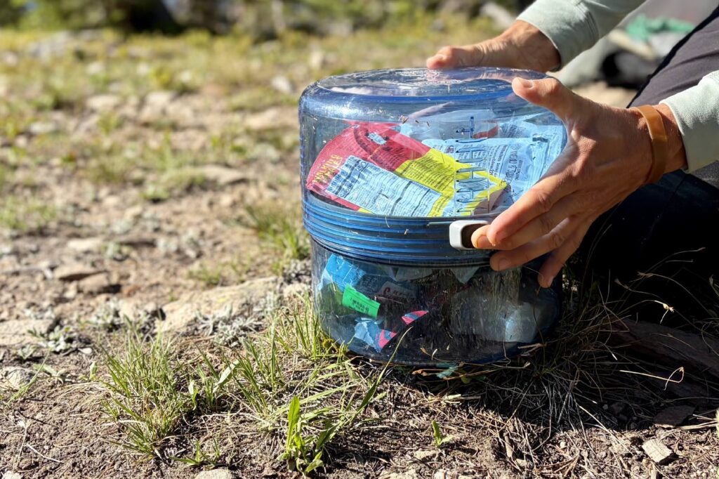 Close-up image of a hiker pressing the locking mechanism on a bear canister.