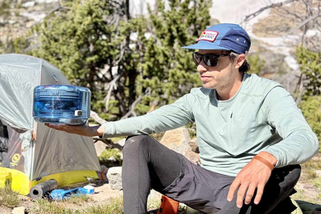 A hiker holds a compressed bear canister in an outstretched arm.