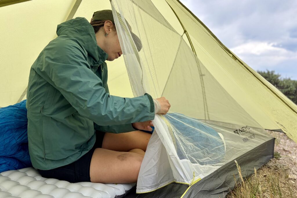 a hiker sits in a tent and ties back the mesh door