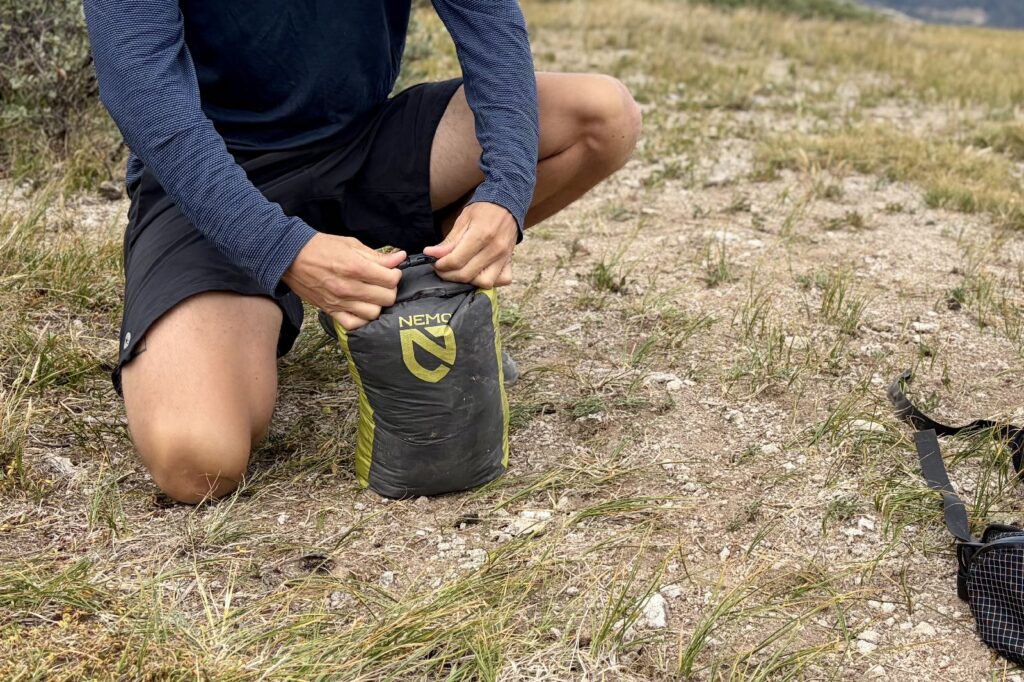a close up of a hiker snapping the roll top closure of a backpacking tent stuff sack