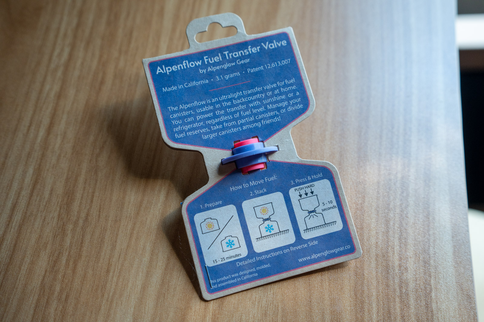 A blue and pink plastic fuel transfer product in a cardboard display card on a wood table.