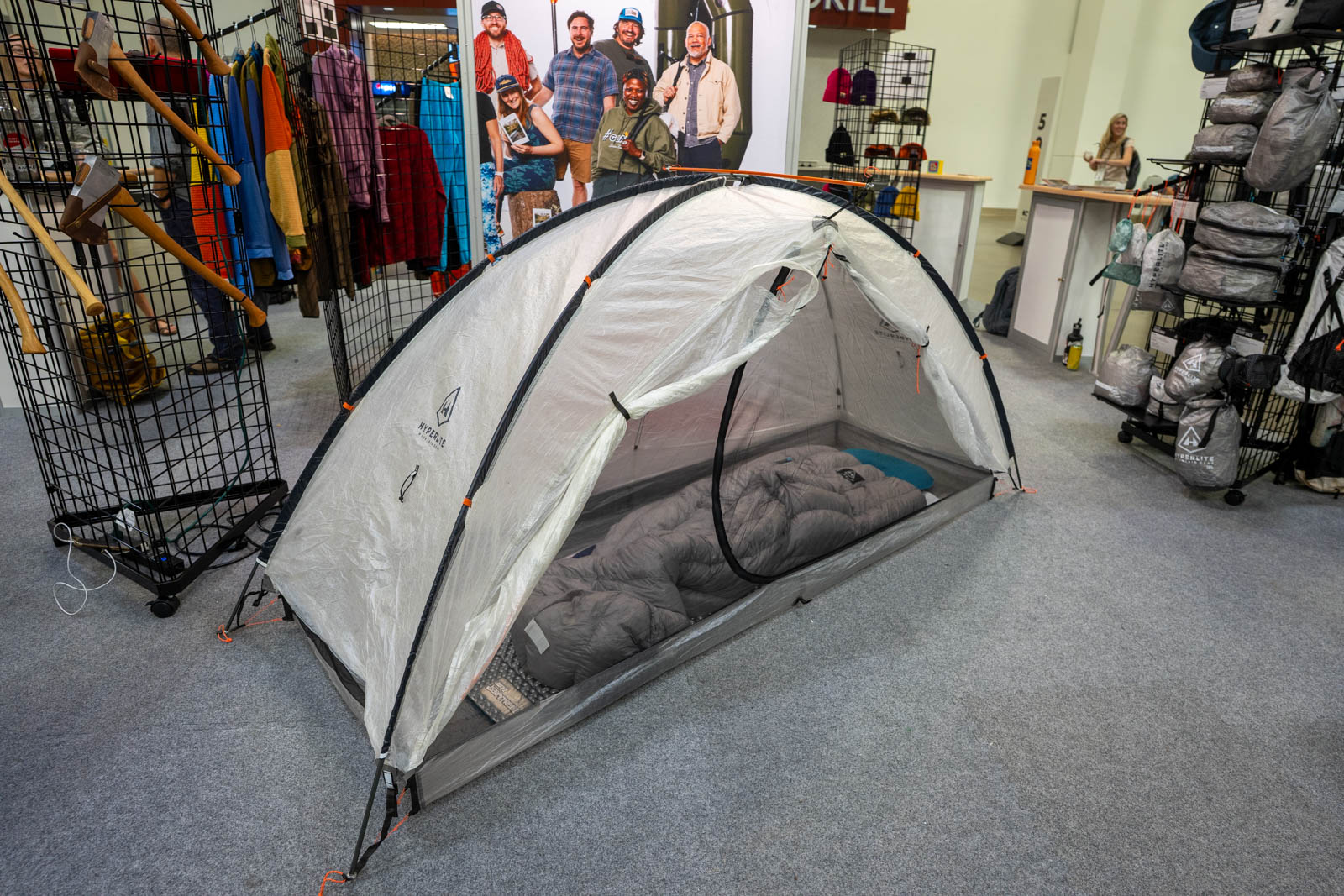 A white backpacking tent sits on the floor of a trade show.