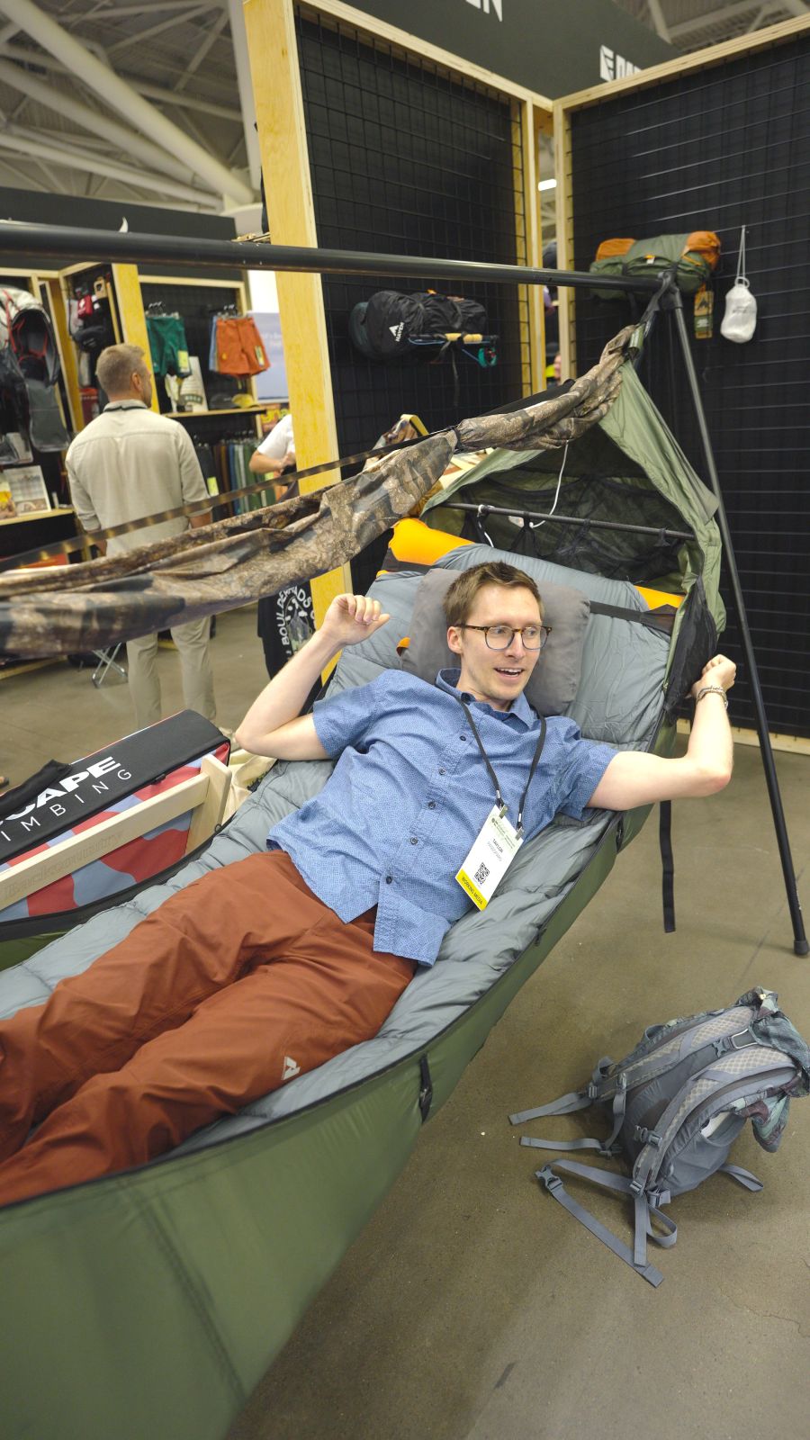 A man lies in a hammock on a trade show floor.